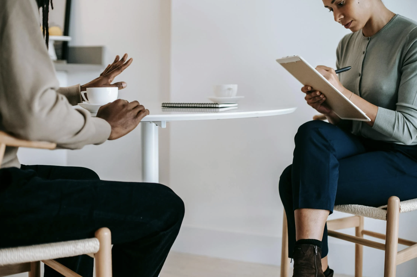 Behavioral health clinician taking notes while speaking with a patient during a counseling session at a small table.